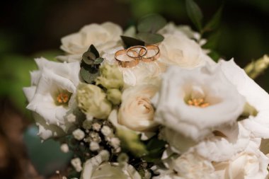 Yakından bakınca zarif altın alyanslar sergileniyor. Beyaz bir buket üzerinde dinleniyor. Sevgi sembolleriyle klasik bir düğün temasını temsil ediyor.