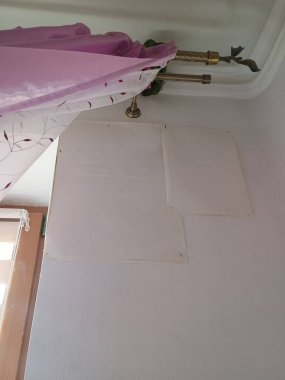 Işıl ışıl aydınlatılmış bir ev içi köşesinde, kısmen koruyucu kağıtlarla kaplı, yeni yamanmış bir duvar, pembe kumaş ve antika pirinç mum tutacaklarına bitişik, son zamanlarda ev geliştirme çabalarını ortaya koyuyor.