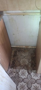 İhmal edilmiş bir banyo köşesinde kirli fayans döşeme, su lekeli duvar boyası ve çürümeyi gösteren döküntü birikintileri görülüyor.