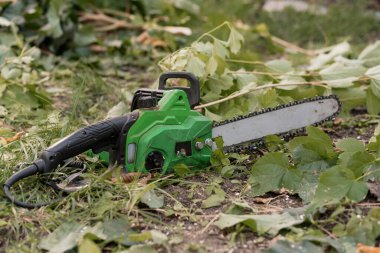 Elektrikli testere, ağaçları kestikten, arka bahçeyi temizledikten, peyzaj ve alet bakımını yaptıktan sonra çimenli bir bahçede yaprak ve dallar arasında uzanır.