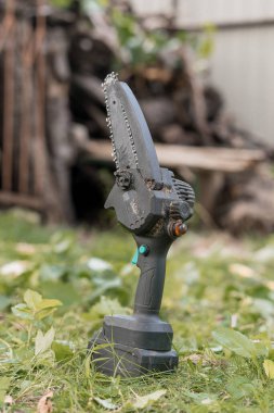 Yakın plan çekimde yeşil çimlerin üzerinde dinlenen kablosuz elektrikli testere kullanılıyor. Bu da bahçenin bakımı için ahşap kesme gücünü gösteriyor.