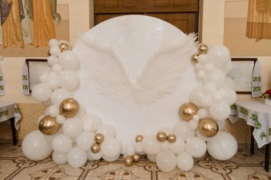 Bu resim, altın aksanlı süslerle süslenmiş, düğün resepsiyonları ve kutlama etkinlikleri için mükemmel beyaz melek kanatlı bir balon kemeri içeriyor.