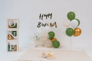 Ahşap bir blok, yeşil ve altın renkli balon çelengi ve parti davetiyeleri ve promosyon malzemeleri için ideal, bir tepeli küçük bir pasta.