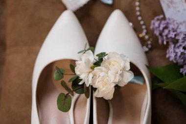 Kırsal ahşap bir yüzeyde zarif çiçekler, inciler ve leylaklarla süslenmiş beyaz düğün ayakkabıları sergilenen güzel bir düğün sahnesi.
