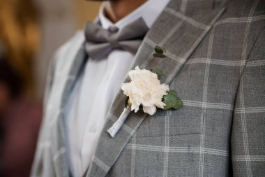 Yakın plan bir damat gri kareli ceket yakasına takılmış narin bir karanfil yaka çiçeği, somut bir düğün zarafeti ve resmi moda