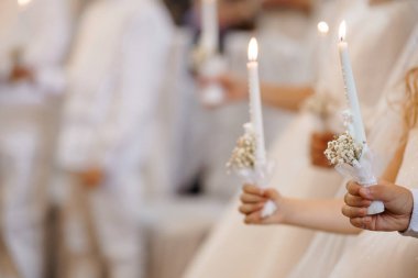 Bir Ortodoks Hıristiyan düğününde, ellerinde bebek nefesiyle süslenmiş mumlar tutan, geleneksel beyaz giysiler giyen, inancı, saflığı ve dini mirası simgeleyen, yumuşak bir an.