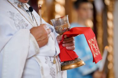 Doğu Ortodoks rahibi, dini bir tören sırasında kırmızı bezle sarılı altın bir kadeh tutuyor. Kutsal nesne cemaati simgeler, ayrıntılı cübbeler ve ruhani bağlılığı gösterir.