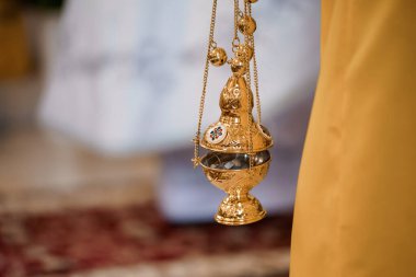 Yakın plan bir resimde, Ortodoks Hıristiyan kilisesi ayininde etkin olarak kullanılan, tütsü dumanı, kutsal ayinleri ve sarı cüppeleri gösteren güzel bir altın sansür merkezi resmediliyor.