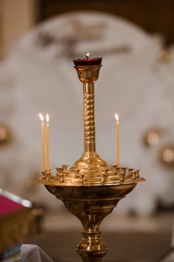 Yakın plan çekimde, kilisenin içinde bir kaç mum tutan süslü bir altın şamdan sergileniyor. İnancı, bağlılığı ve huzur dolu dini törenleri simgeliyor.