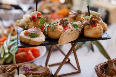 Bir yemek organizasyonunda deniz ürünleri, crostini sosları ve canlı sebze garnitürlerinin yer aldığı koyu bir tabakta sunulan çeşitli gurme kanepelerin yakın çekimi.