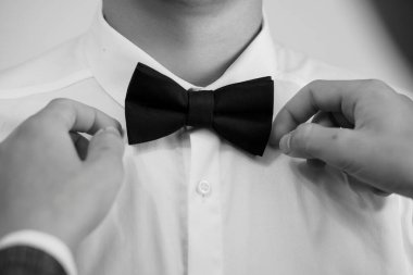 Yakın çekim, siyah papyonu beyaz bir gömlek üzerine dikkatlice bağlarken, sofistike, olay hazırlığı ve klasik stili temsil eder.