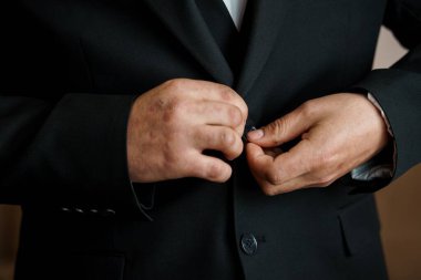 Yakın plan çekimde siyah ceketinin düğmelerini ilikleyen bir adam resmedilmiş, profesyonel bir estetik işi resmedilmiş. resim zarafet ve incelik taşır.
