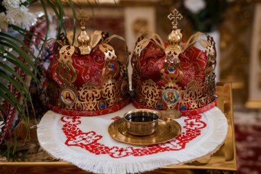Kutsal Ortodoks Hıristiyan evlilik ritüelini sembolize eden kırmızı bir kase ile süslenmiş altın düğün taçlarının ayrıntılı görüntüsü.