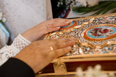 Kilise ayini sırasında elinde madalyalı altın bir İncil kitabı tutan bir Ortodoks rahibinin yakın plan fotoğrafı. Karmaşık işçiliği ve ruhani atmosferi vurguluyor.