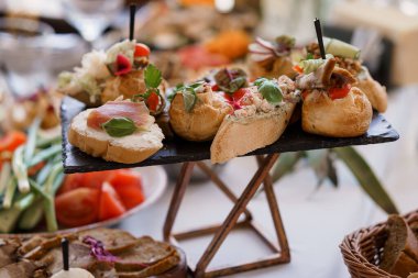 Bir yemek organizasyonunda deniz ürünleri, crostini sosları ve canlı sebze garnitürlerinin yer aldığı koyu bir tabakta sunulan çeşitli gurme kanepelerin yakın çekimi.