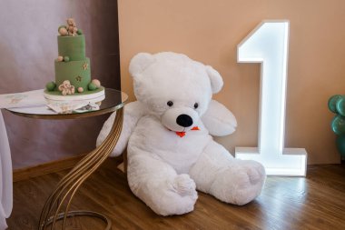 Büyüleyici bir ilk doğum günü partisi hazırlığı büyük beyaz bir oyuncak ayı ve katmanlı pastel yeşil pasta. Yıldızlar ve badem kurabiyeleriyle süslenmiş, altın rengi bir numaralı fon.