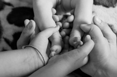 Yeni doğmuş bir bebeğin ayaklarını kucaklayan ebeveynlerin şefkatli anları. Tek renkli aile fotoğrafı, sevgi, koruma ve yeni hayatlar sergileniyor.