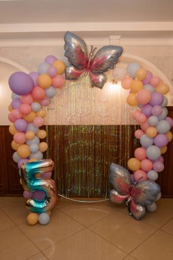 Neşeli bir beşinci yaş günü partisi düzeninde kelebek balonlarıyla süslenmiş pastel renkli bir balon ve 5 numaralı büyük folyo balonu festival havası yaratıyor.