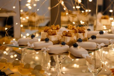 Ceviz ve yaban mersinli bireysel cheesecake ısırıklarının yer aldığı güzel bir tatlı masası, yanında beyaz jöleli pastalar, yumuşak, sıcak, ışıldayan ışıklarla parlıyor.