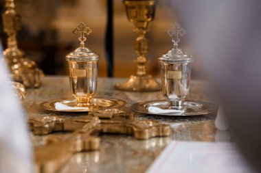 Kutsal Ortodoks komünyon gemilerinin yakından görüntüsü suyla dolu, bez bir sunakta altın tepsiler ve zengin dekore edilmiş bir kilisede kadehlerle süslenmiş.