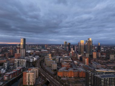 Günbatımında Manchester ufuk çizgisini gösteren büyüleyici bir hava manzarası, aydınlanmış Deansgate Meydanı yüksek binaları ve şehir merkezi çevresi de dahil olmak üzere modern kent mimarisini vurguluyor..