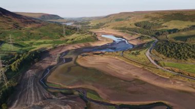 Sersemletici hava görüntüleri kuraklığın Derbyshire 'daki Woodhead Reservoir' daki etkisini gözler önüne seriyor. Düşük su seviyeleri ve kuru zemin ortaya çıkıyor. Bu kavrulmuş manzara, iklim değişikliği endişelerini vurguluyor.