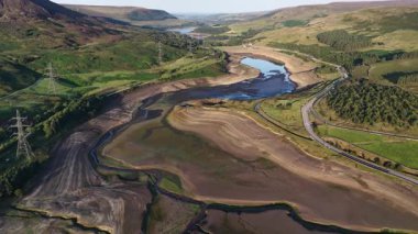 Sersemletici hava görüntüleri kuraklığın Derbyshire 'daki Woodhead Reservoir' daki etkisini gözler önüne seriyor. Düşük su seviyeleri ve kuru zemin ortaya çıkıyor. Bu kavrulmuş manzara, iklim değişikliği endişelerini vurguluyor.