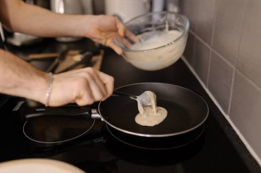 Bir adamın sıcak tavaya krep hamuru karıştırdığı yakın plan bir fotoğraf. Yüksek kalite fotoğraf