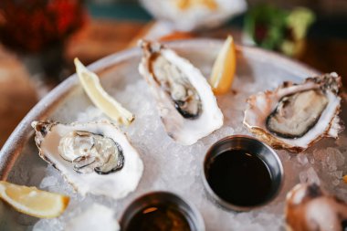 Limon dilimleri ve soslarla ezilmiş buz üzerinde servis edilen soğuk istiridye tabağının yakın plan görüntüsü, seçici bir odaklı kırsal deniz ürünleri restoranında çekildi. Yüksek kalite fotoğraf