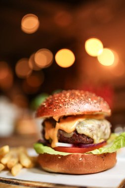 Eritilmiş çedar peynirli, gevrek marullu ve domatesli ağız sulandıran çizburger sıcak restoran ışıklarının altında kızartılmış çörek. Yüksek kalite fotoğraf