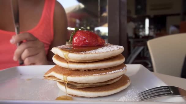 在煎饼上倒入蜂蜜 再加上新鲜的草莓 为咖啡店特写镜头中的小女孩准备 早餐吃甜点 — 图库视频影像