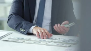 İş adamı yakın planda oturan dolarları sayar. Anlaşmadan büyük kar