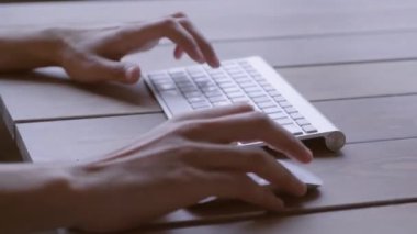 Adam ahşap masadaki kablosuz bilgisayar klavyesine yazı yazıyor. Uzak çalışma yeri