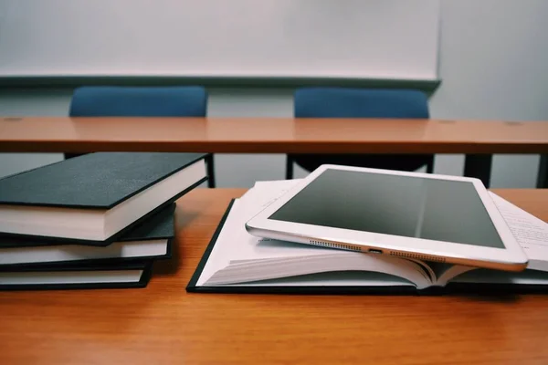 Ders kitapları ve tablet bilgisayarı sınıfın ahşap masasının üstünde yakın plan çekimde. Modern eğitim kavramı