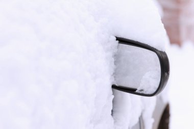 Arabanın tek dikiz aynası karın altından görülebilir. Park halindeki bir yolcu vagonu yoğun kar yağışı nedeniyle açık bir otoparkta karla kaplıydı.