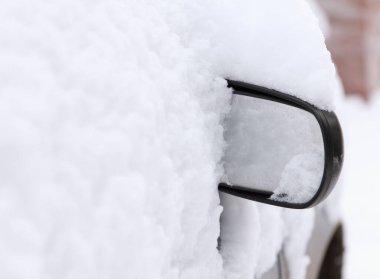 Arabanın tek dikiz aynası karın altından görülebilir. Park halindeki bir yolcu vagonu yoğun kar yağışı nedeniyle açık bir otoparkta karla kaplıydı.