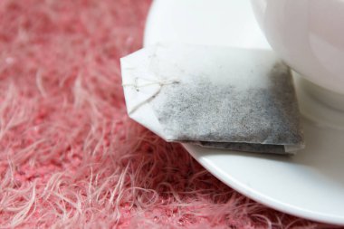 Çay poşeti çay fincanının üstünde, bir bardak kaynar suyun yanında, pembe örülmüş yün bir arka planda nefis kokulu çay demlemek için.