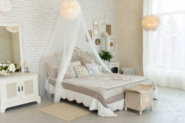 Açık renkli mobilyaları, dört posterli yatağı, tüylü lambaları, odunlu küçük şöminesi, dinlenmek ve uyumak için rahat ve modern bir yeri olan rahat geniş bir yatak odası.