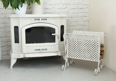 Ahşap ve kömürün üzerinde küçük güzel bir şömine, metal işlemeli paleti olan beyaz bir oda. Kışın bir odayı ısıtmak için harika bir yol.