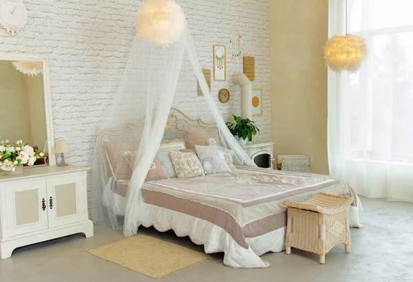 Comfortable large simple bedroom with light-colored furniture, four-poster bed, feather lamps, small fireplace on wood, cosy modern place for rest and sleep