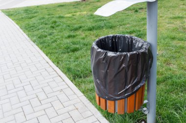 Çöp torbasıyla dolu bir çöp kutusu halka açık bir yere, bir parka yerleştiriliyor. Kaldırıma yakın bir yerde..