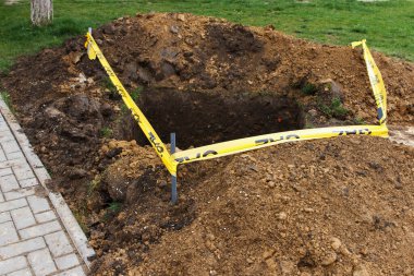 Toprağa kazılmış kare bir çukur, halka açık kaldırımın yanında ve tehlike işareti olarak sarı bir kurdele ile çevrili. Toplum hizmeti çalışır, yeraltındaki sorunları ortadan kaldırır