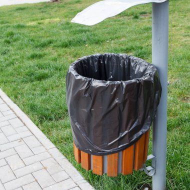 Çöp torbasıyla dolu bir çöp kutusu halka açık bir yere, bir parka yerleştiriliyor. Kaldırıma yakın bir yerde..