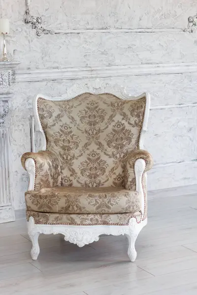 Beautiful new classic style armchair sits next to a decorative fireplace and candles in a hall with a stylish interior