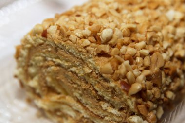 Yumuşak odaklı beyaz arka plan, tatlı konsepti üzerine yerleştirilmiş, kremalı, gerçekçi tarzda, fındık kaplı pasta rulo yakın çekim