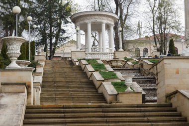 Süslü balyaları ve bitkileri olan büyük taş basamaklar manzaralı bir şehir parkında klasik beyaz bir kubbeye çıkıyor.