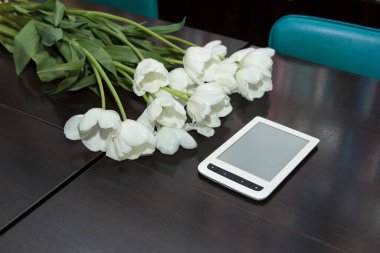 Seyirciler arasında bir buket beyaz lale ve siyah ahşap bir masada beyaz bir elektronik okuyucu.