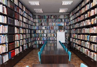 CHISINAU, MOLDOVA - 14 Mart 2025; Uzun ahşap masalar, mavi sandalyeler ve seramik zemin üzerindeki kitaplarla dolu modern kütüphane iç mimarisi, eğitim ve bilgiyi simgeliyor