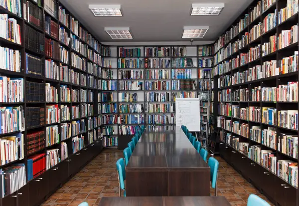 CHISINAU, MOLDOVA - 14 Mart 2025; Uzun ahşap masalar, mavi sandalyeler ve seramik zemin üzerindeki kitaplarla dolu modern kütüphane iç mimarisi, eğitim ve bilgiyi simgeliyor