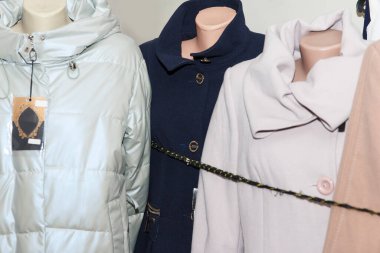 Bej, mavi ve beyaz da dahil olmak üzere çeşitli kışlık paltolar bir mağazanın içindeki mankenlerde sergilenmekte, moda tarzları sergilenmektedir.